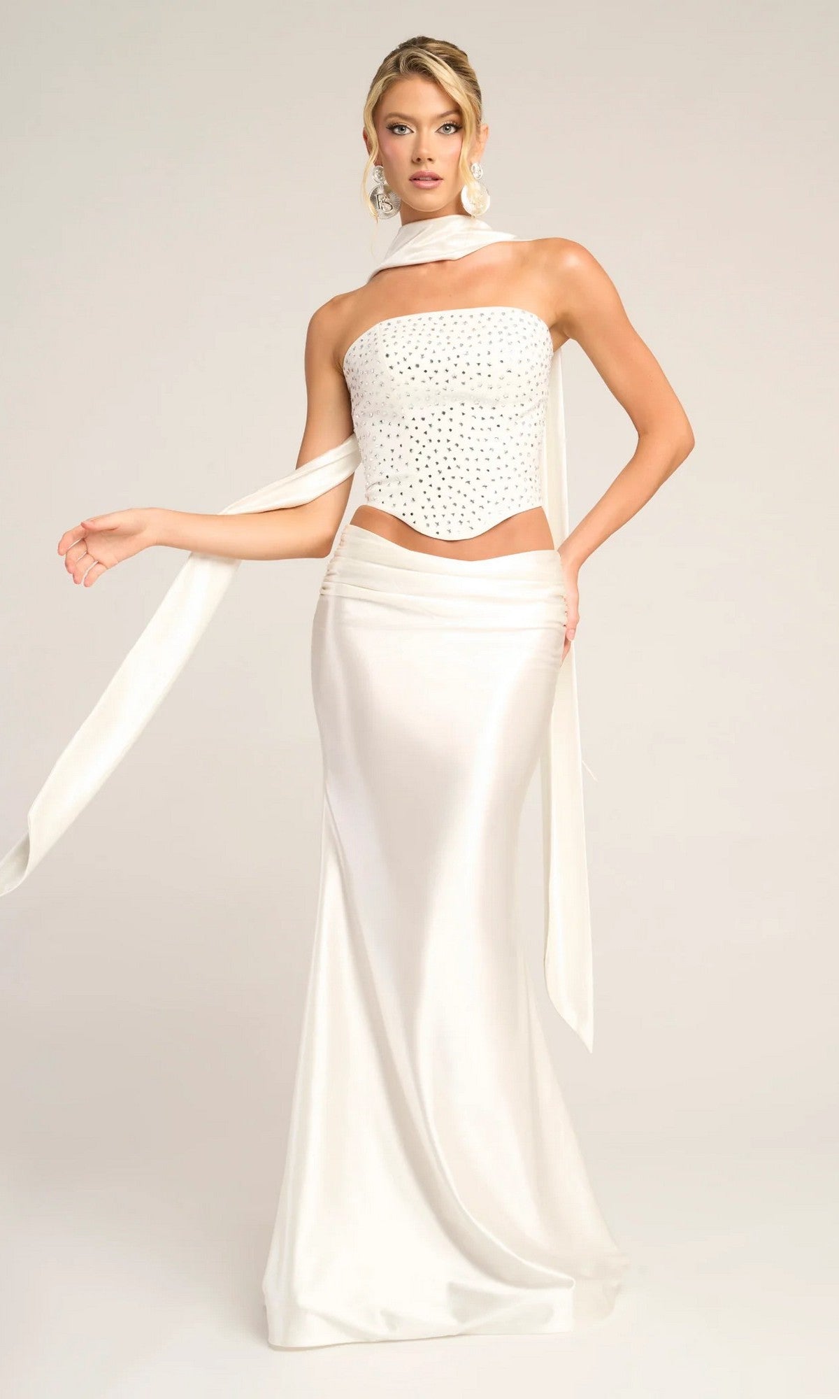 A woman models the Portia and Scarlett PS26042 long formal dress in white, featuring a strapless beaded corset top and matching satin skirt, posing against a plain light background.